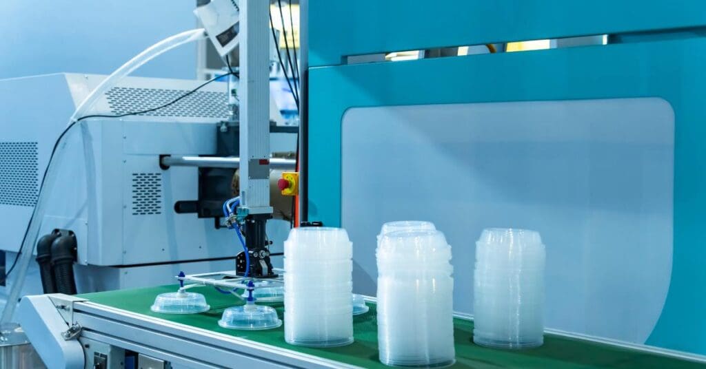A close-up of a stack of polypropylene food containers on the conveyor belt of a plastic injection molding machine.