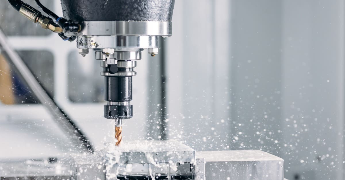 CNC milling machine cuts a metal workpiece as coolant sprays around the rotating tool inside an industrial workshop.