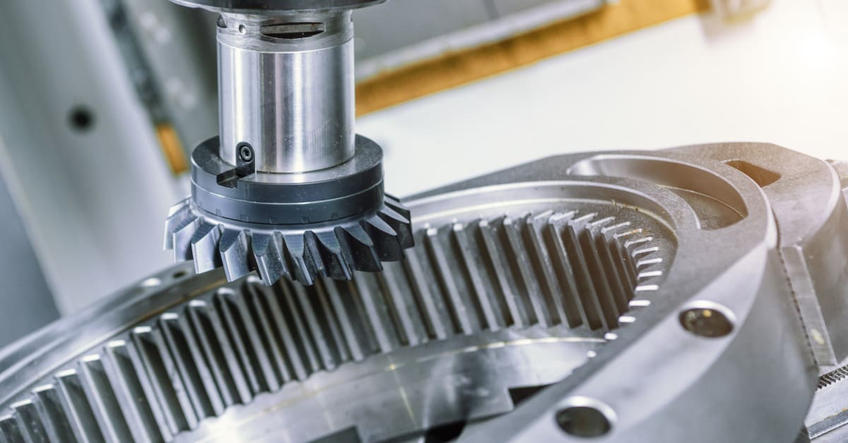 Industrial cutting tool works above a circular steel gear component with deep internal teeth inside a machine.