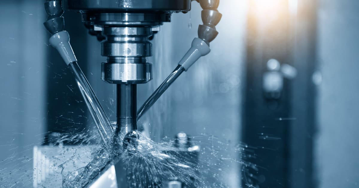 Close-up of a CNC machine cutting a metal component while streams of coolant splash around the spinning tool.